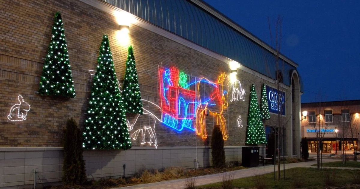  Illuminated holiday display on a brick building wall featuring trees, animals, and a colourful horse-drawn sleigh.